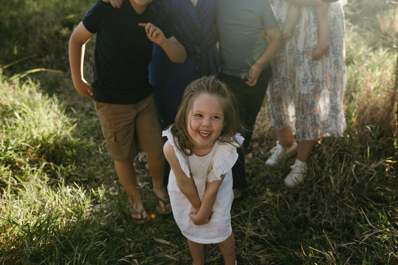 A little girl laughing in the sunset light with her family behind her