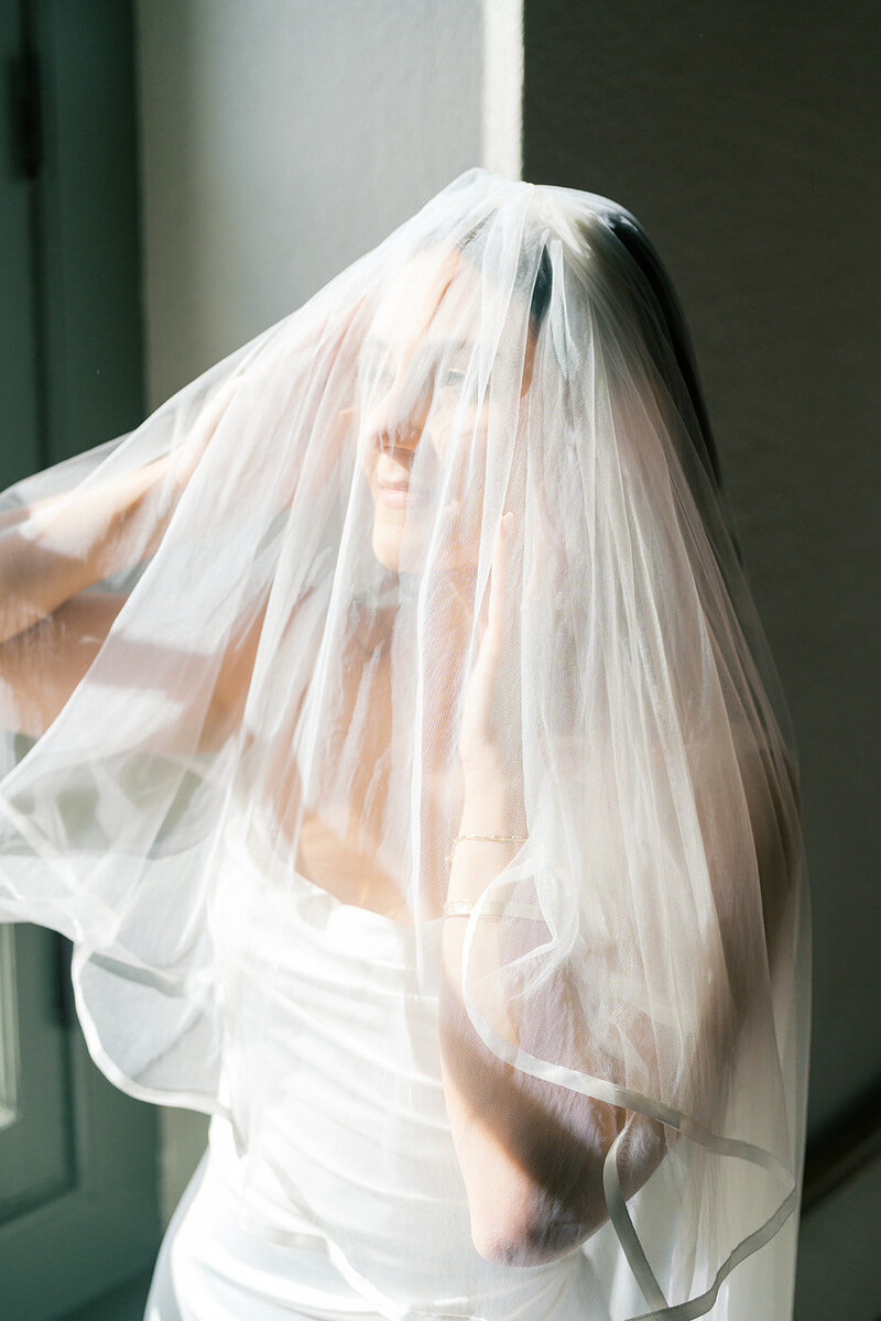 Bride looks into window light with her hands under ethereal veil inside Crane Cottage at Jekyll Island Resort