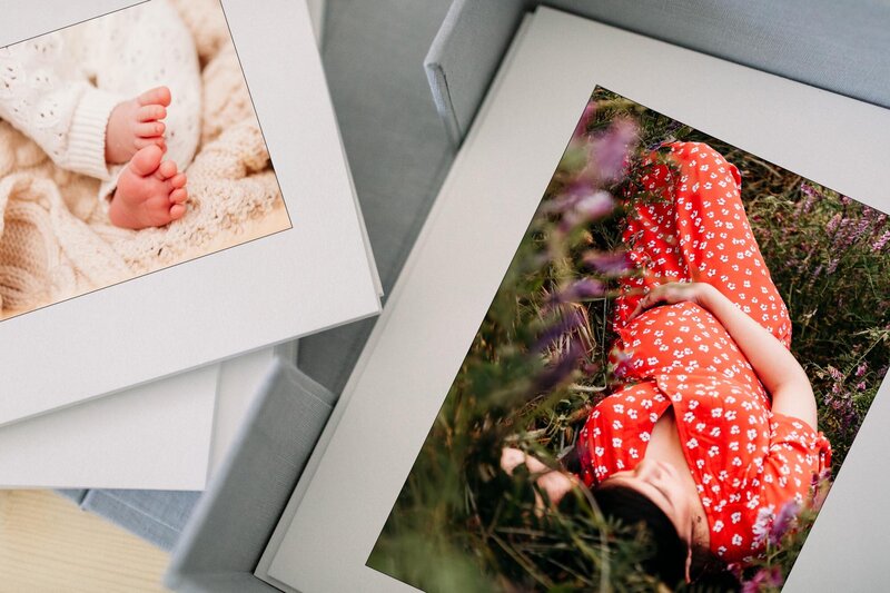 Mockup of a photo album featuring two photos by Delaware maternity photographer, kristi.  Left side of the album is a photo of a newborn baby's feet, and right is a pregnant woman laying in a field of purple hairy vetch while cupping her baby bump