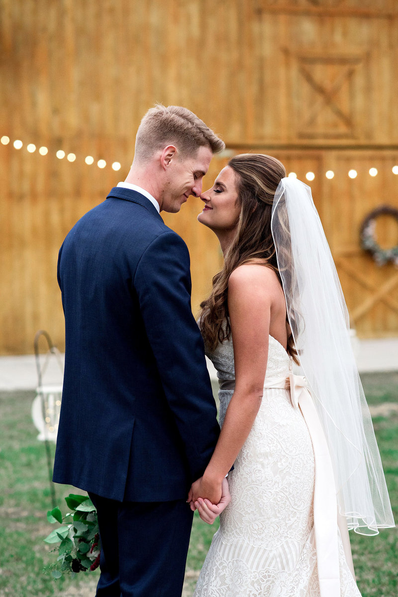 Winter wedding, couple standing outside, nose to nose and holding hands with the barn in the background