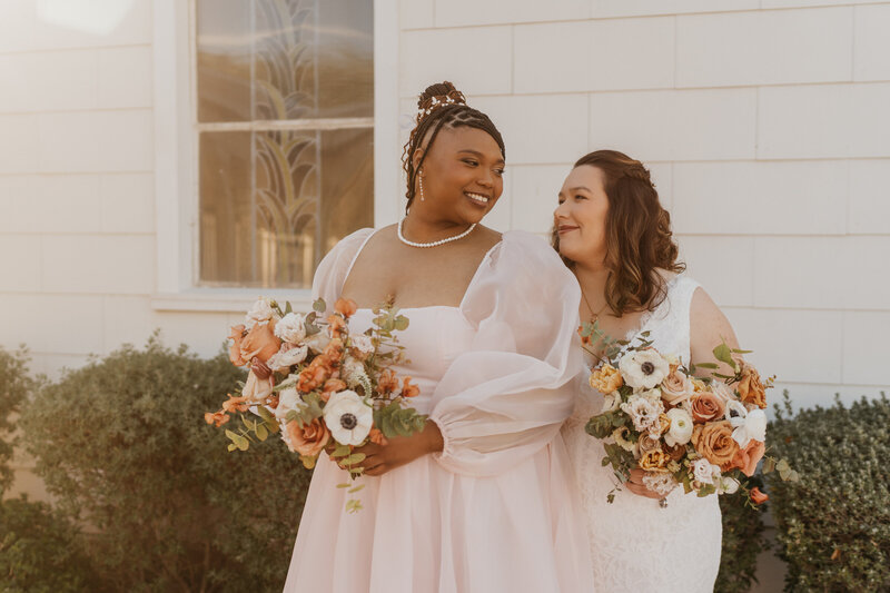 A newlywed couple standing one behind the other smiling at each other 