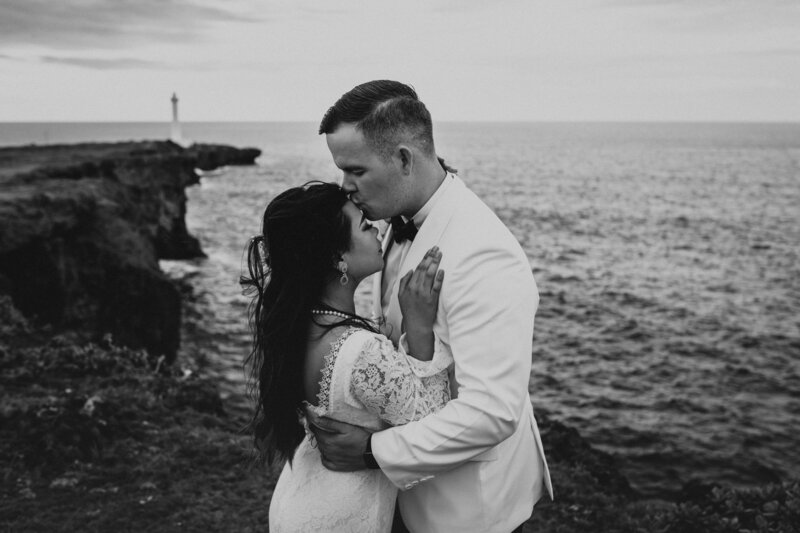 black n white image of J kissing M's head as they hold each other, alongside the cliffs overlooking the ocean