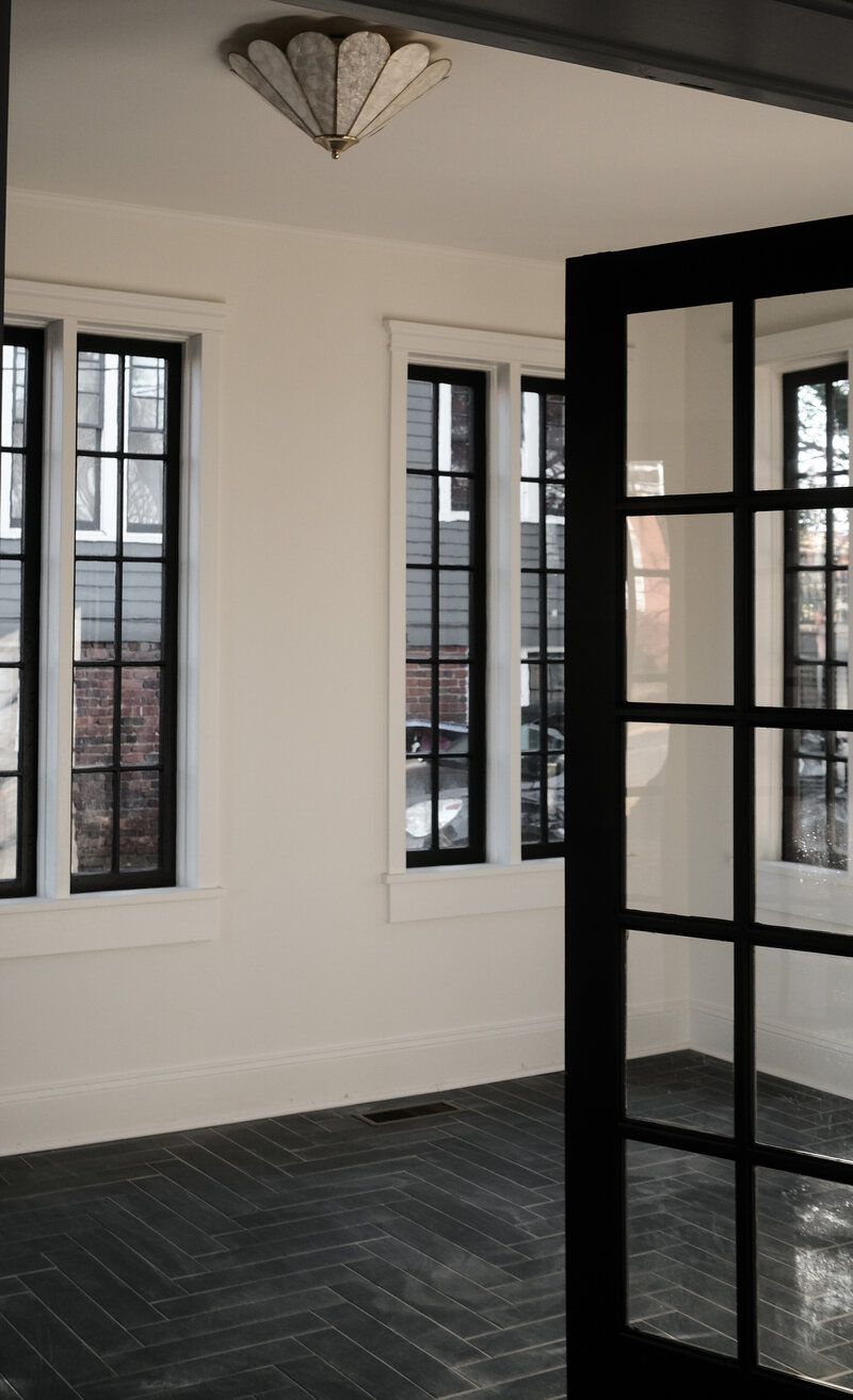 Step into a slice of history with this stunning sunroom design from a 1920's renovation. The symmetrical black double windows create a timeless and elegant look, while the slate herringbone floor adds a touch of texture and depth. The natural light floods the space, creating a warm and inviting atmosphere perfect for relaxing and entertaining. The Anthropologie light fixture adds a modern twist, bringing this space into the 21st century. With a keen eye for design, this renovation seamlessly blends old and new, creating a space that is both beautiful and functional. Get inspired to bring a touch of vintage charm to your own home with this breathtaking sunroom design.