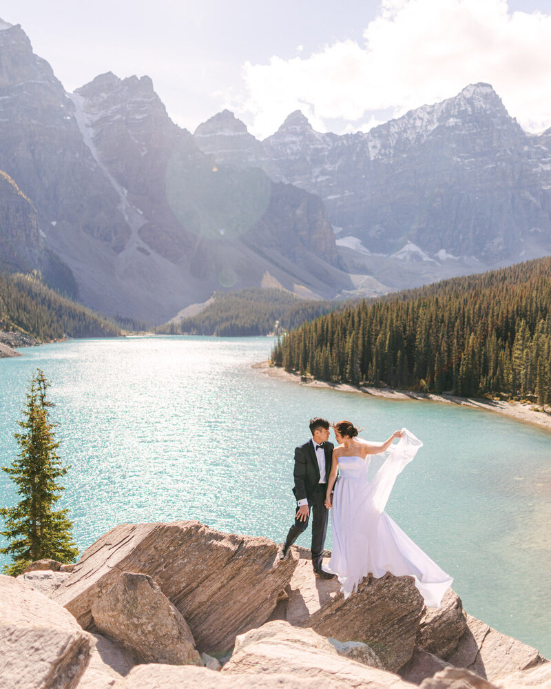 Amid the summer beauty of Moraine Lake, a bride and groom share a heartfelt moment with the towering Valley of the Ten Peaks behind them. The iconic backdrop and vibrant lake reflect the romance and grandeur of their day in the Canadian Rockies.