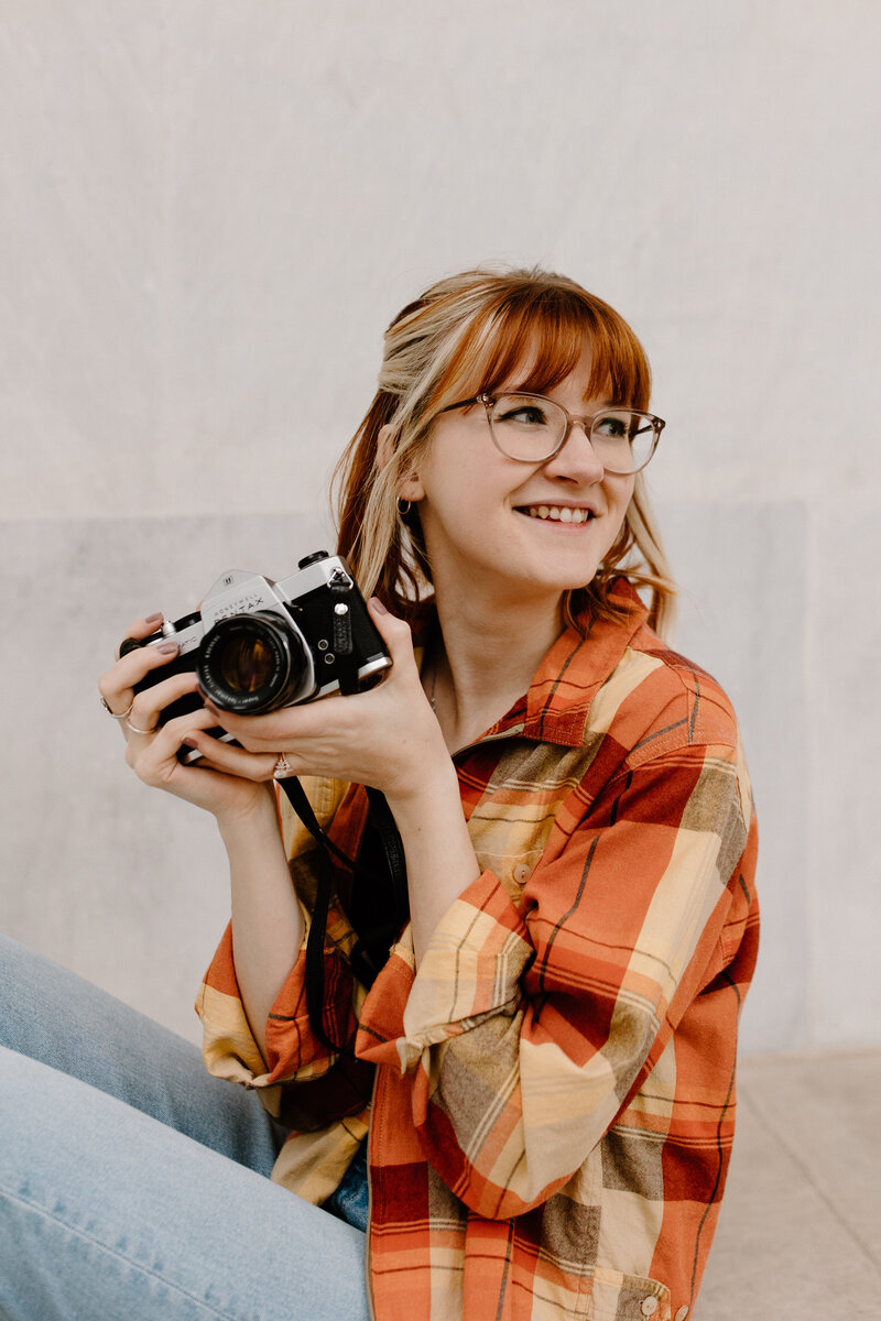 woman smiling while sitting down and holding a large camera