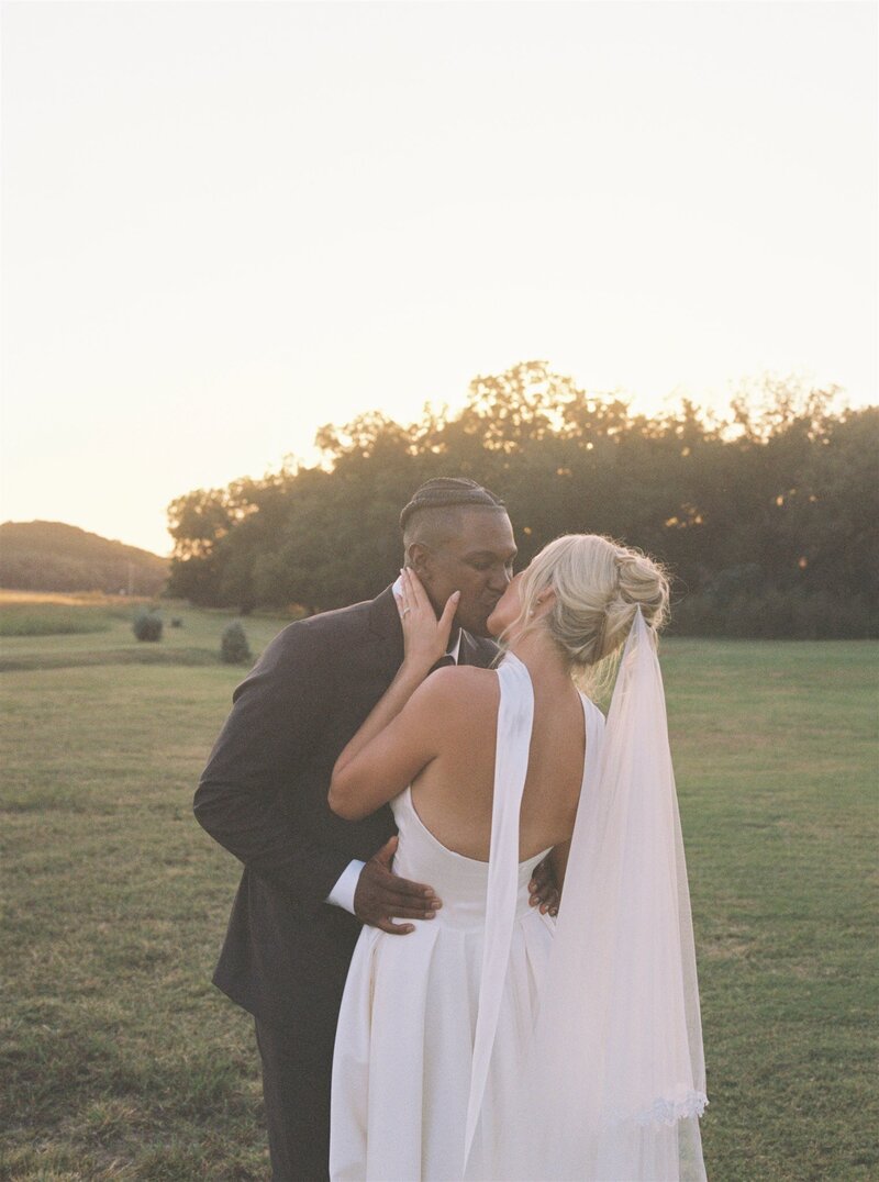 Couple kissing in field post wedding ceremony