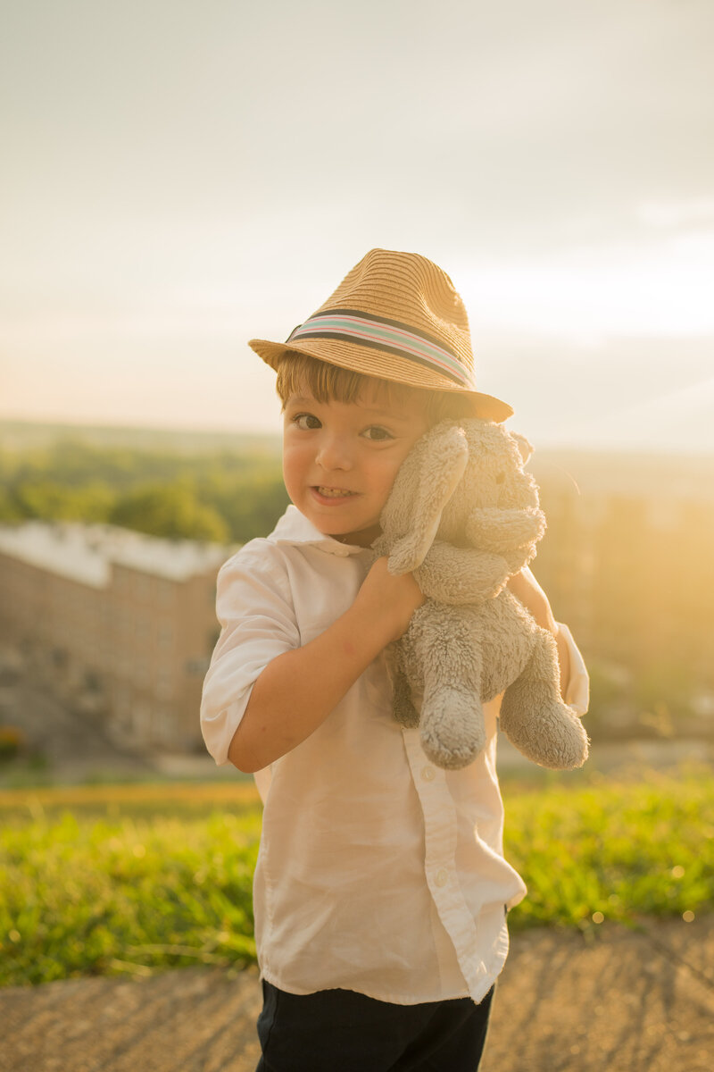 A kid smiles at the camera while holding his stuffed elephant.
