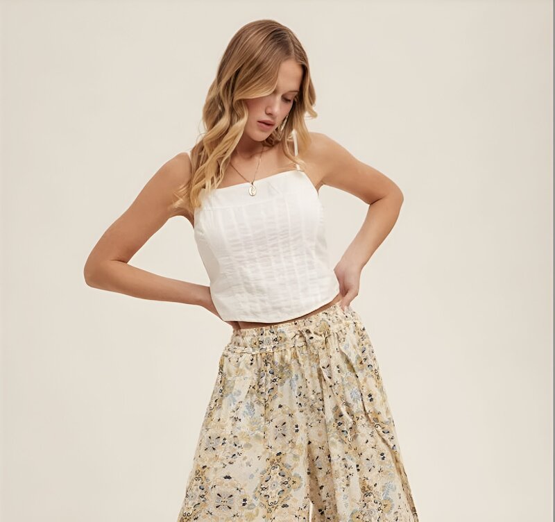 An image of a young woman in her twenties with medium length blonde hair looking down wearing a stylish white tank top with oversized flower patterned flowy pants in delray beach, florida.