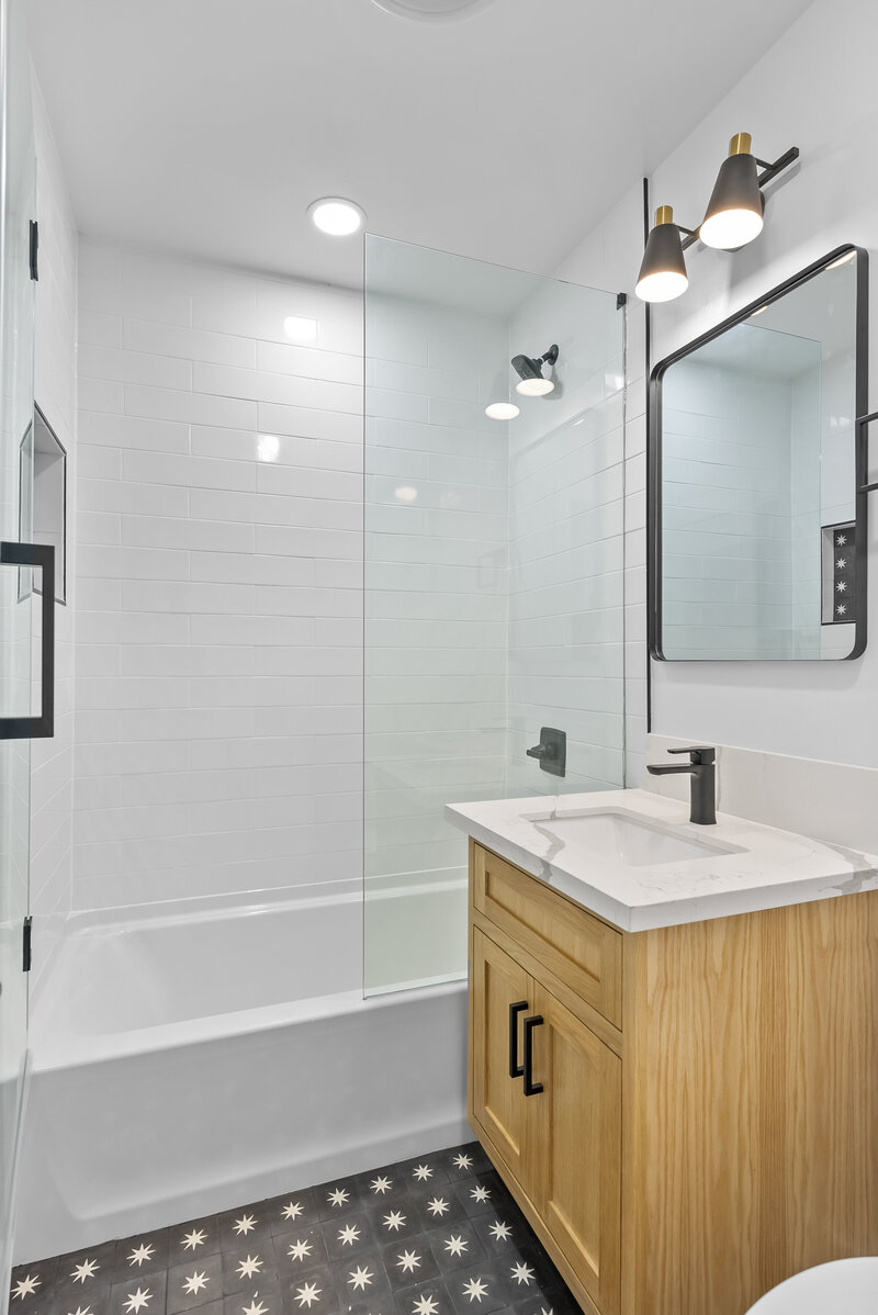 Sleek modern bathroom remodel by AW Development featuring white subway tile walls, wood vanity, matte black fixtures, and star-patterned tile flooring