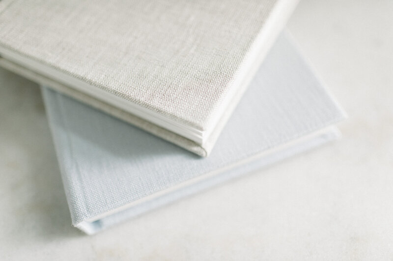 Stack of linen heirloom photo albums in neutral tones, featured as part of a Kansas City photographer’s print product offerings.