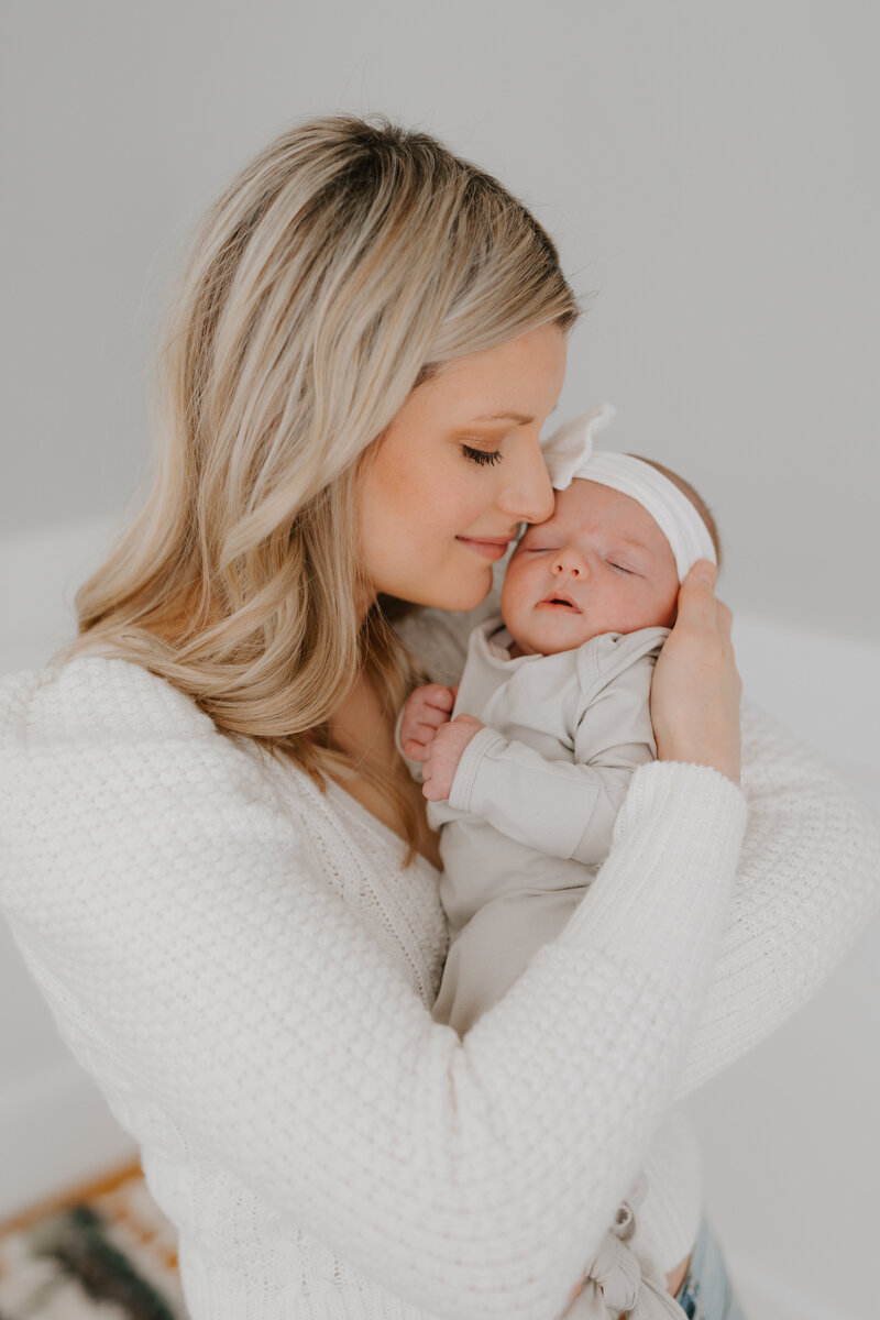 Blonde mother holding newborn baby girl close to her face
