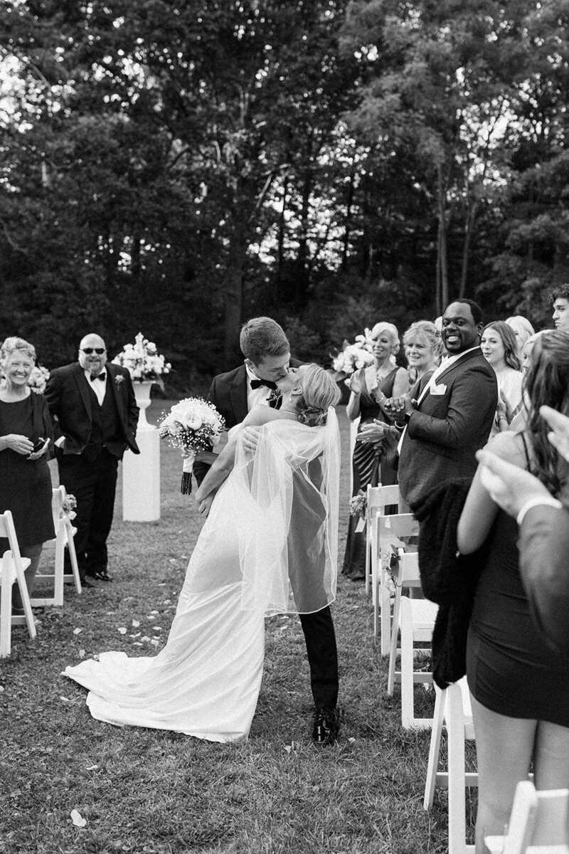 Black and white bride and groom kissing in the aisle after getting married with their guests smiling at them