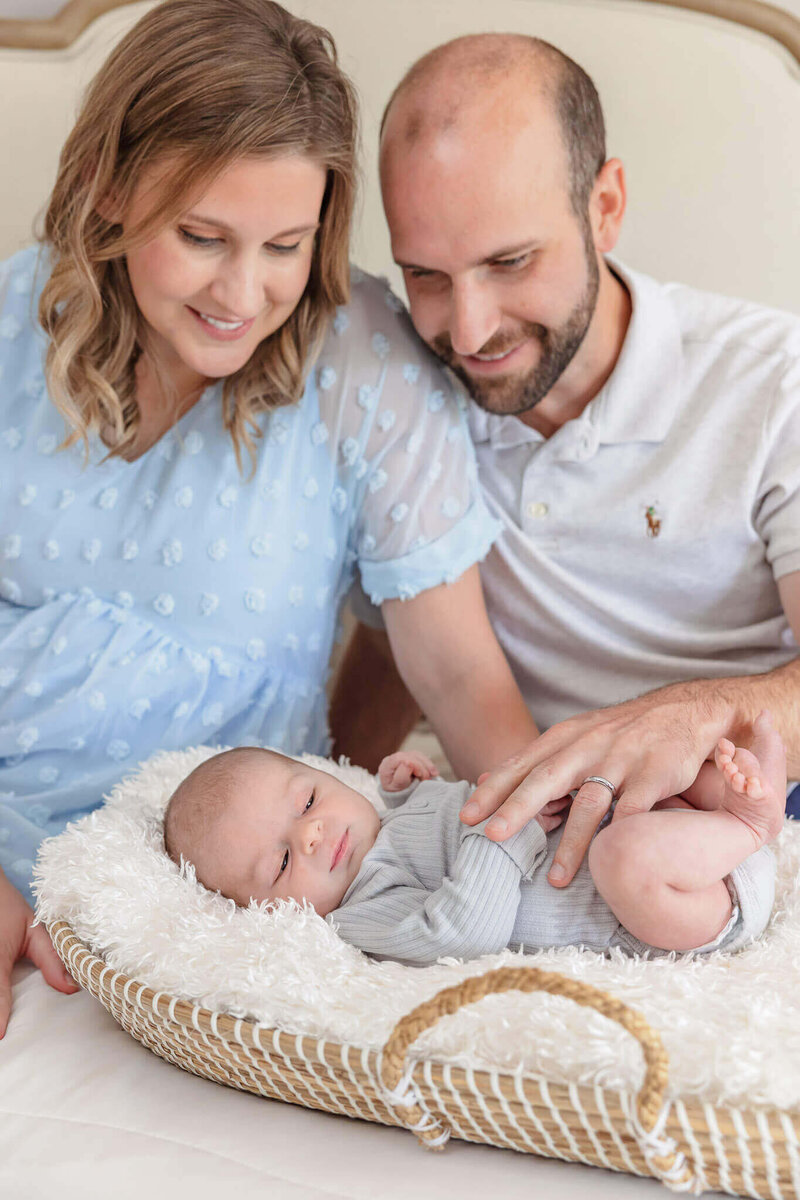 A Northern VA couple sitting in bed and smiling down at their newborn son in a Mose's basket.
