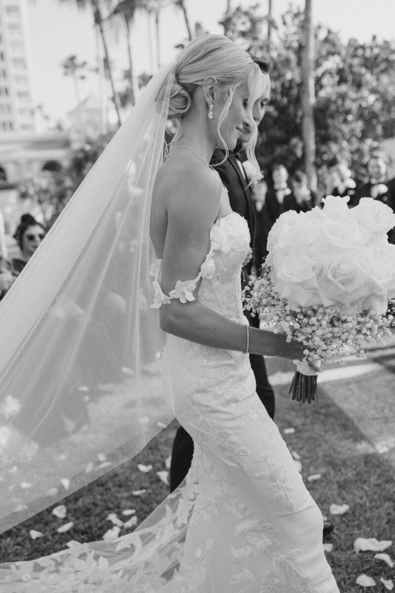 Black and white photo of bride and groom walking with bride holding bouquet of flowers