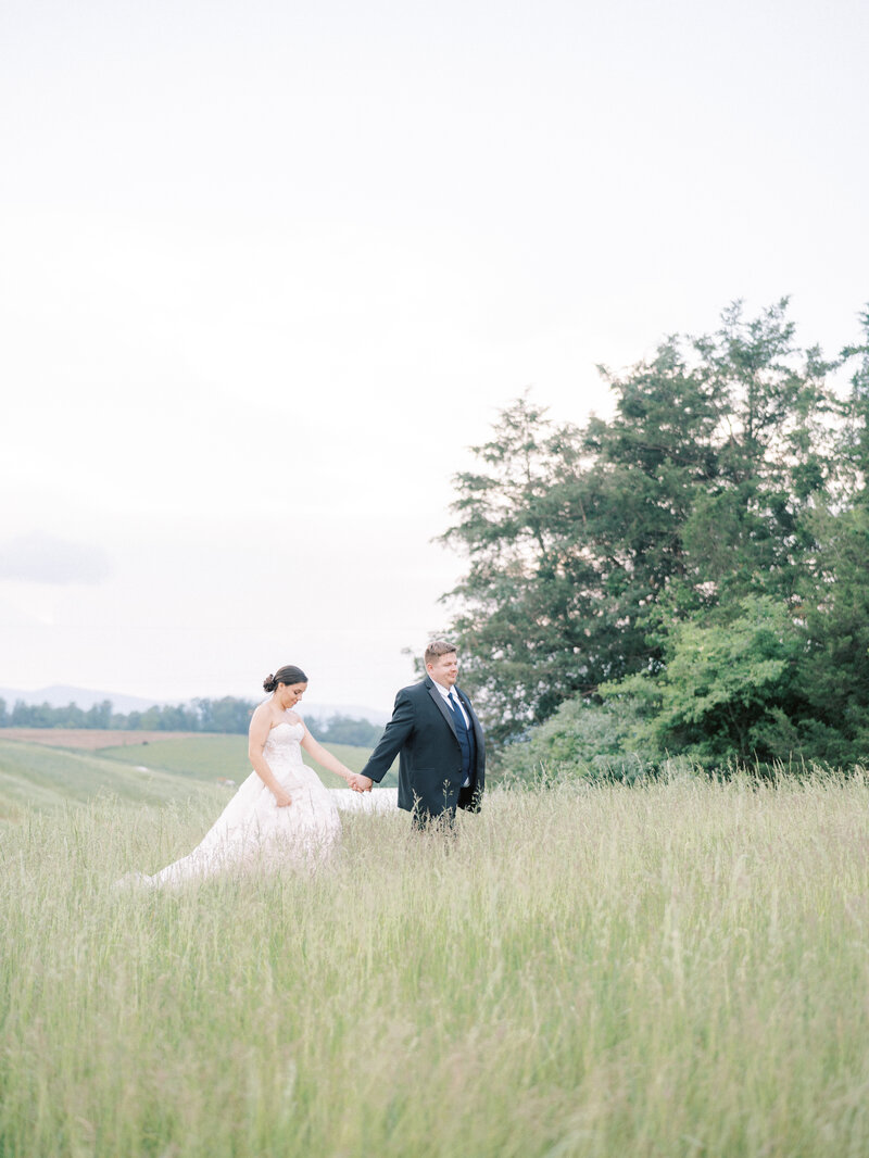 Bride and groom walk hand in hand through a field in a Harrisonburg, Virginia venue
