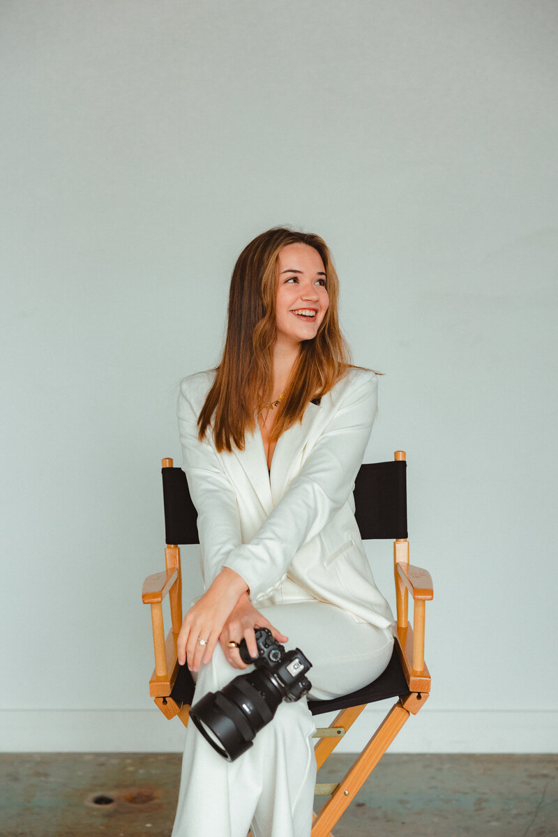 Photographer sitting on a chair, smiling for a headshot.