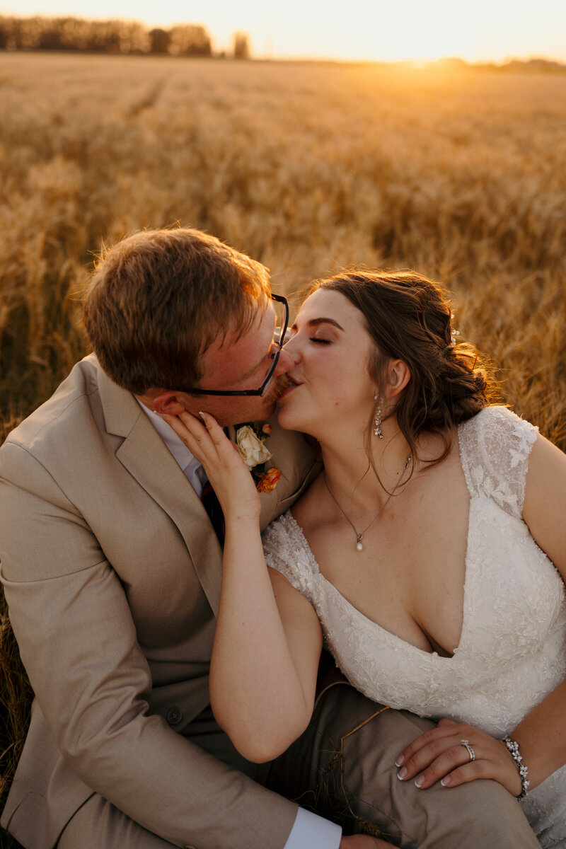 groom kissing bride in sunset field