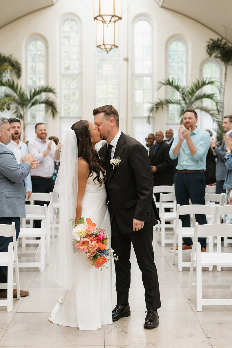 African American bride and brunette groom kiss after ceremony at Piper Palm House in Missouri