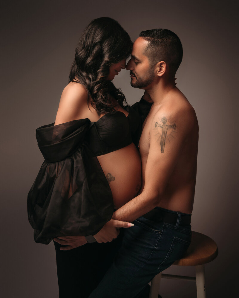 beautiful couple embracing woman's baby bump with dramatic lighting