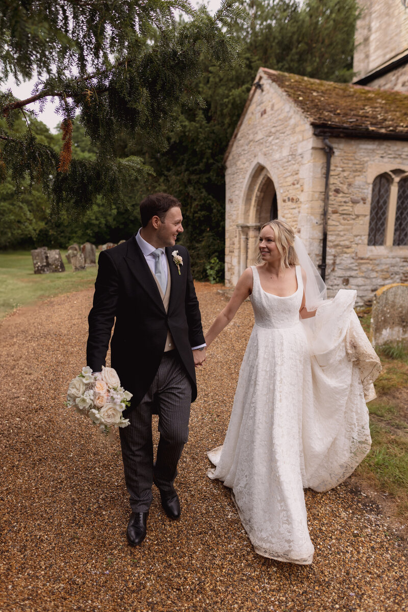 A couple pose with the bride raising the bouquet in the air at their luxury wedding ceremony in the cotswolds