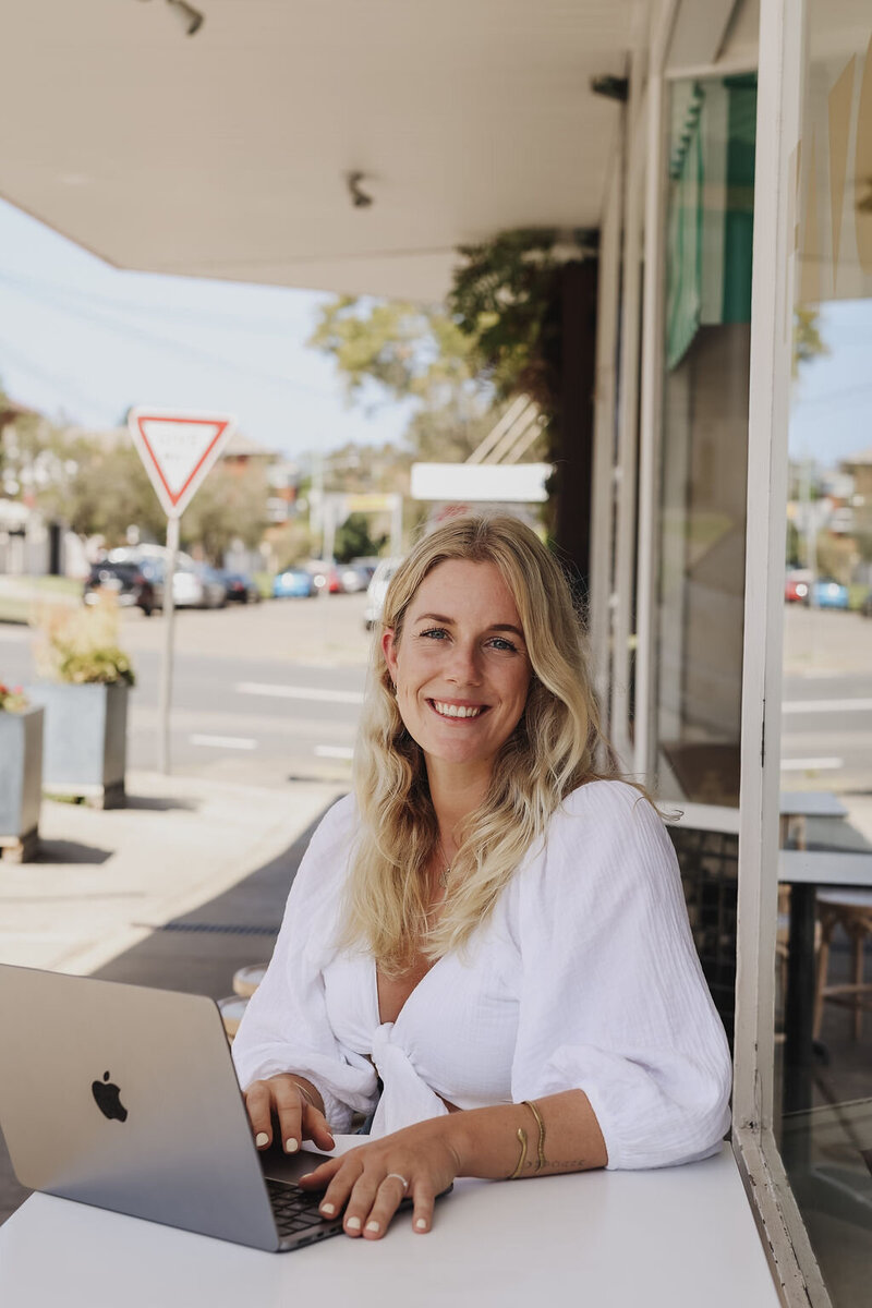 Woman sitting in front of a cafe with her laptop