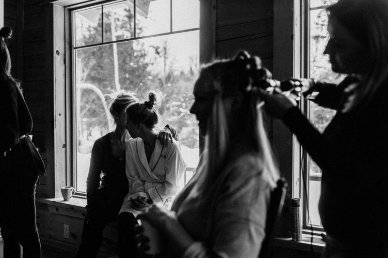 A bride and her bridesmaids getting ready in front of a large window on her wedding day.