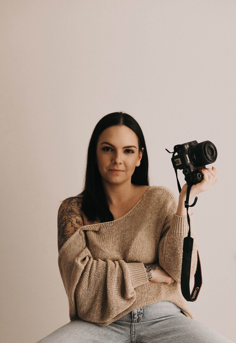 Mullingar photographer with long dark hair and arm tattoos holding a professional DSLR camera