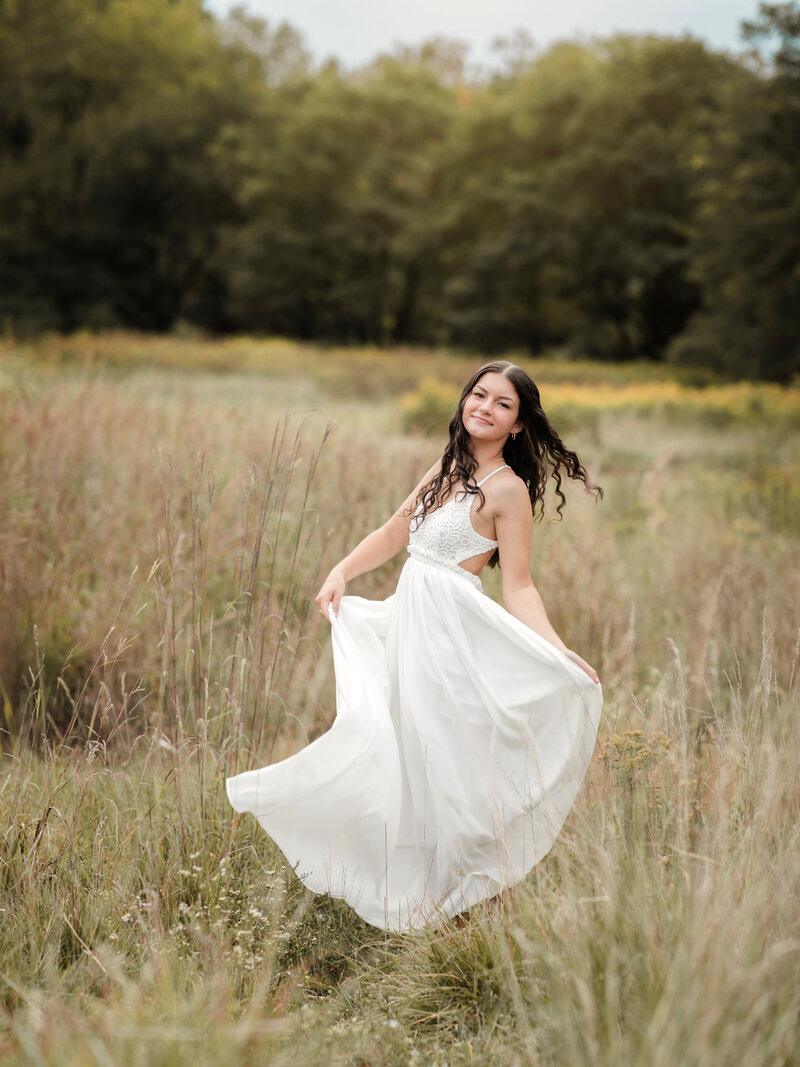 senior girl in white dress twirling in field for senior photos Cleveland family photographer