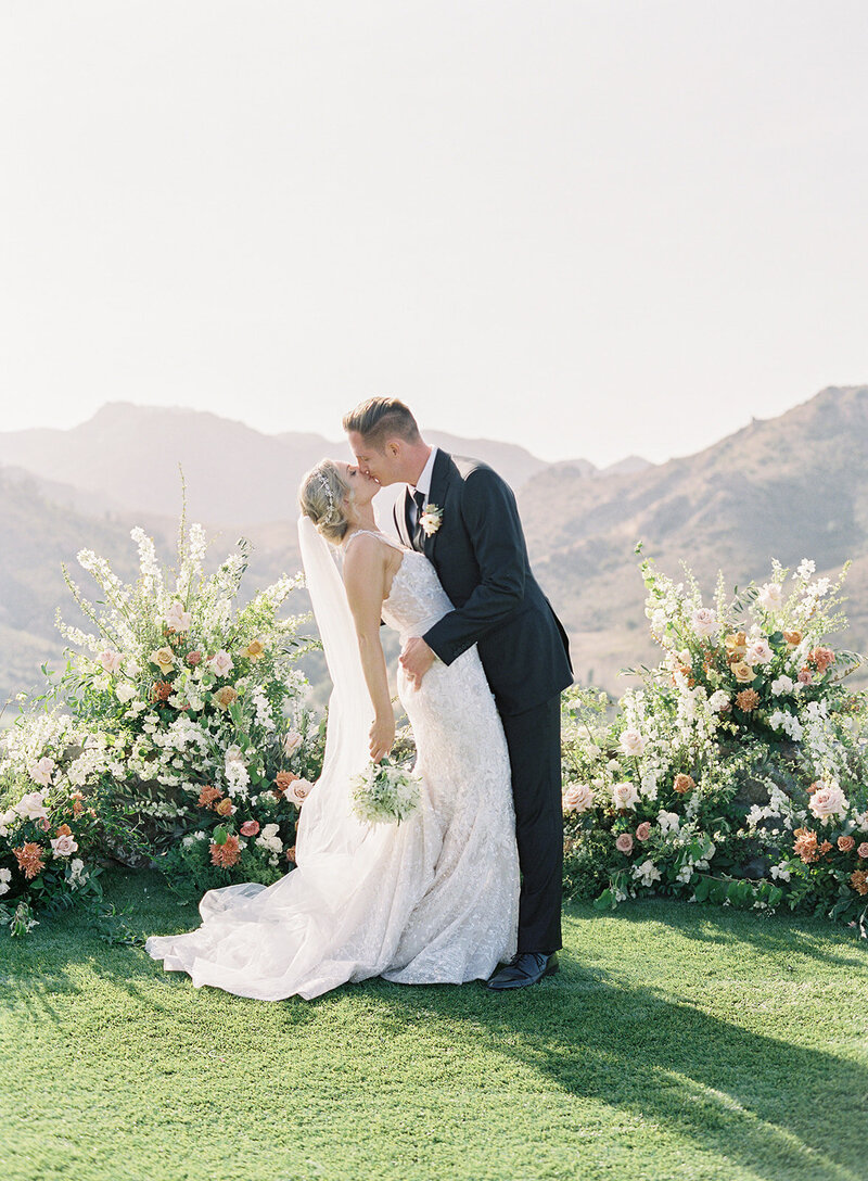 Bride & Groom Kiss with Lush Romantic Wedding Ceremony Floral Installation & View of Malibu Hills