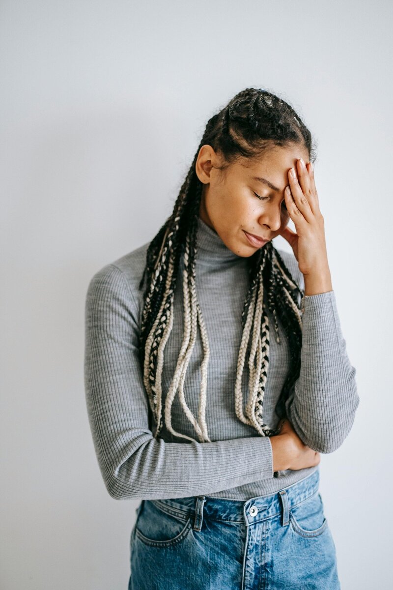 A black woman with braids appears stressed, rubbing her temple
