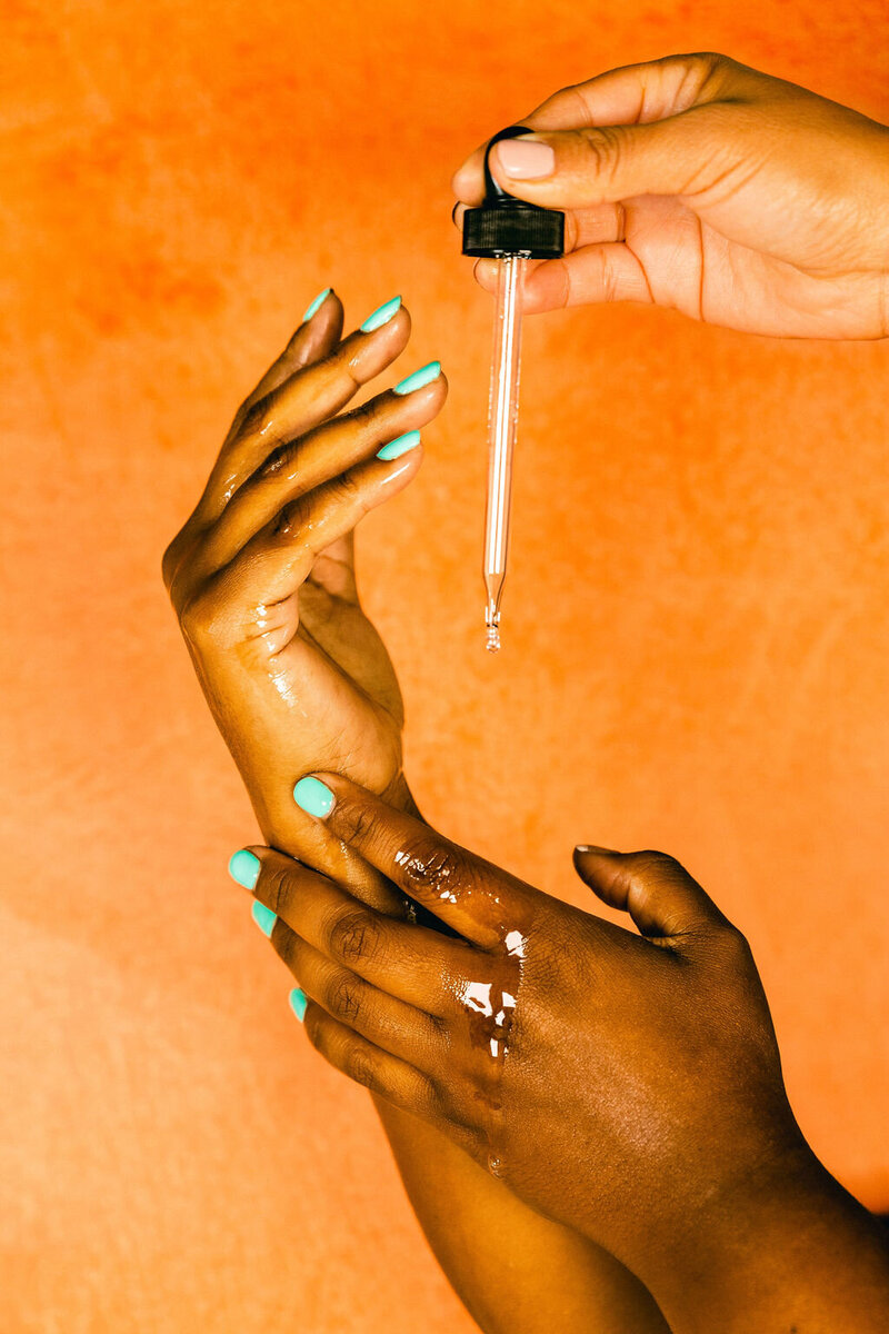 Editorial skincare photography black women oil dripping on hands colorful orange backdrop