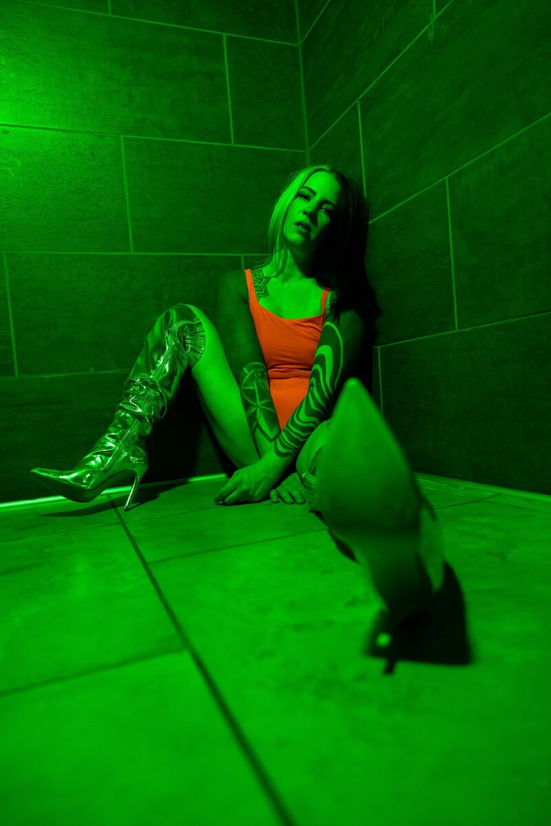 Tattooed Woman Sitting on Floor in Green Lighting With Silver Boot