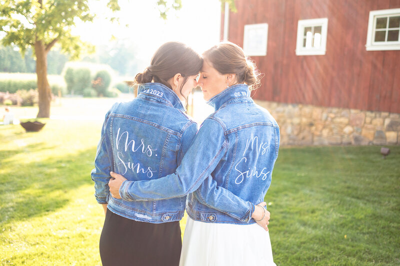 Two brides embrace and hug as sunset after the wedding wearing matching jean jackets