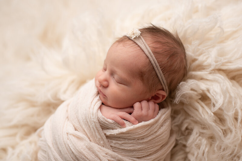 Newborn girl wrapped in white with close up of baby features