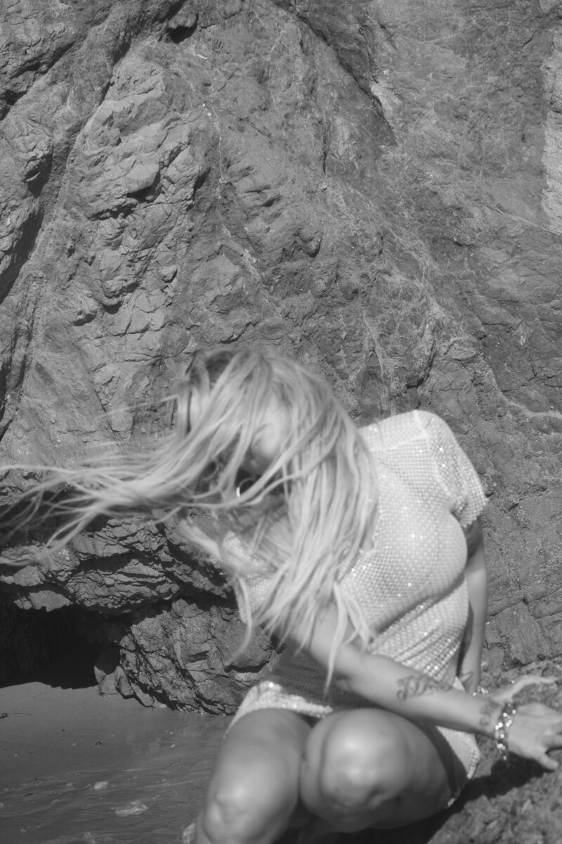 Nicky Lynn dancing on the shoreline in a blue dress, expressing freedom, joy, and emotional release