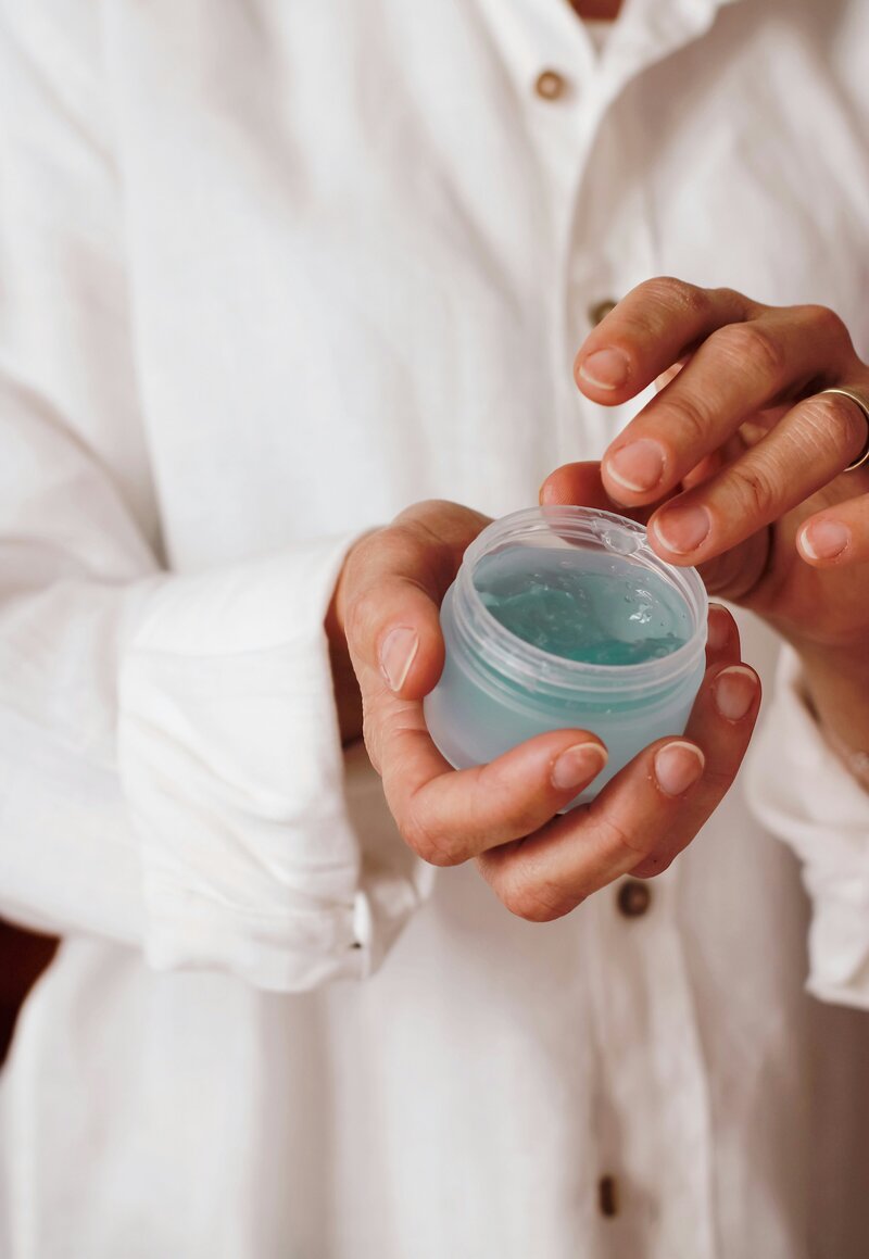 Hands holding a skincare product jar with a blue gel in it
