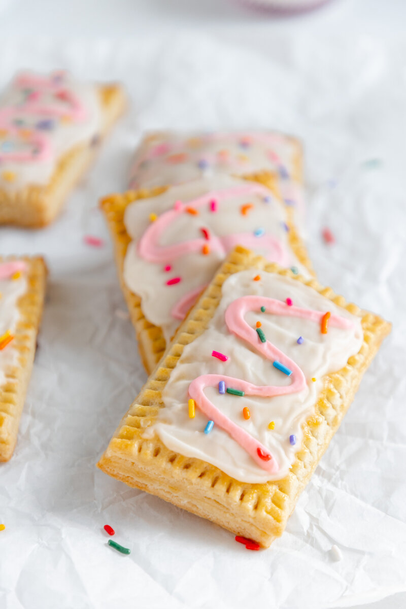 a hand pie decorated with white and pink  frosting and sprinkles
