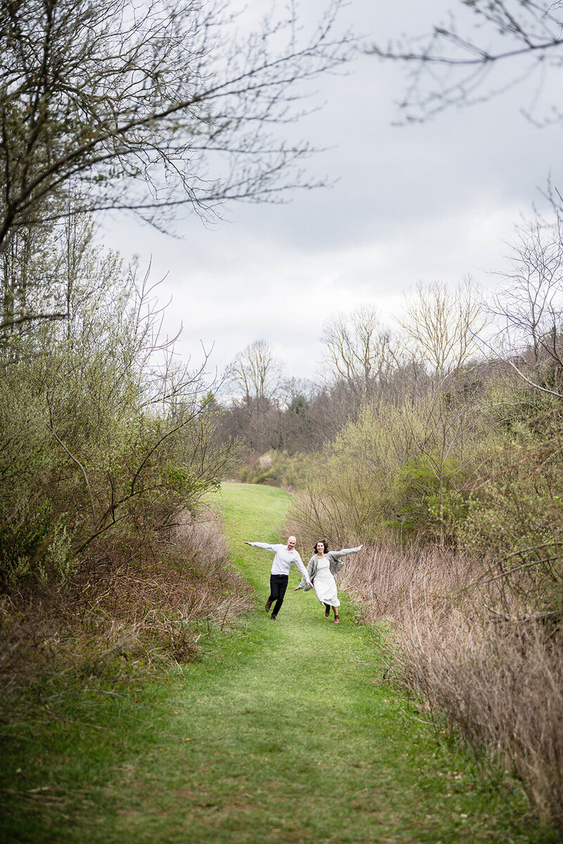 A bride and groom run together smiling widely on a trail at Heritage Park in Blacksburg, Virginia on their elopement day.