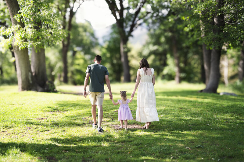 Photo of a a family with a toddler walking away from the photographer in a green setting.