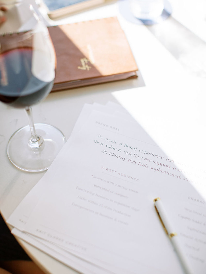 hand written notes, a pen, and a glass of red wine on a table