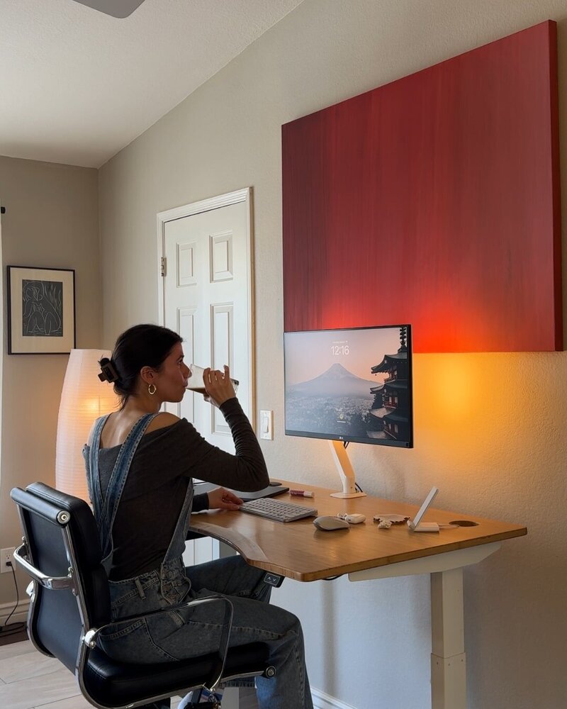 female influencer virtual assistant sitting in a home office drinking coffee typing on her laptop