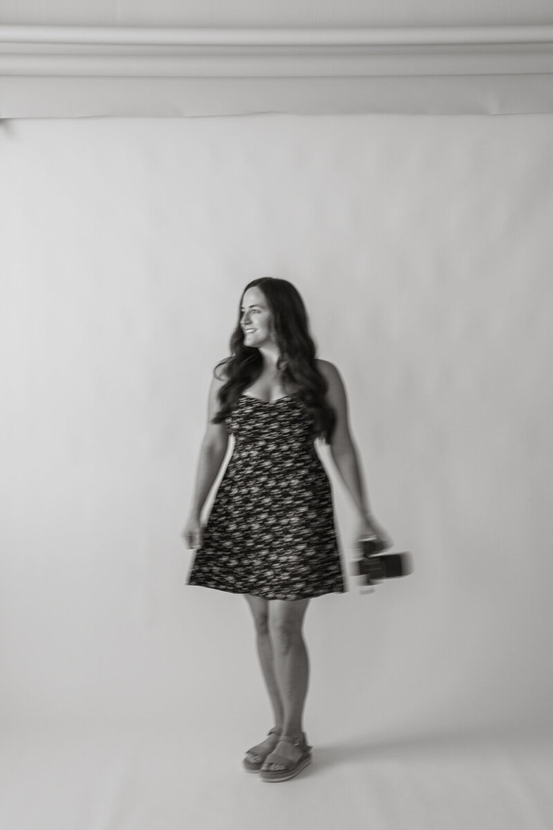 Stephanie Wilson sits in a rattan chair on a white photography backdrop while smiling at the camera