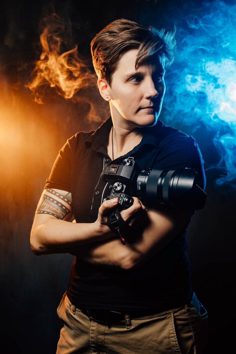 A photographer holding a camera with blue and orange smoke behind them 