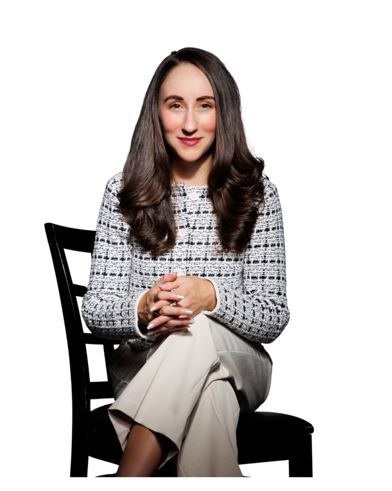 A confident woman in a tweed blazer and cream trousers sitting on a black chair, smiling with hands clasped — radiating authority and grace in a branding photo.