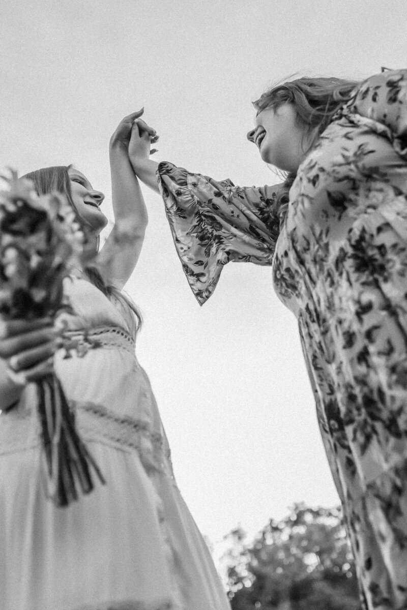 Lawrence KS photographers capture senior girls in flower field as they hold hands and smile at each other