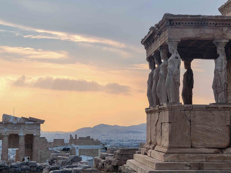 The Erechtheion’s Caryatid columns overlooking Athens at sunset, with the cityscape stretching to the mountains beyond ©Stephanie Dosch | theViatrix Greece Private Luxury Travel