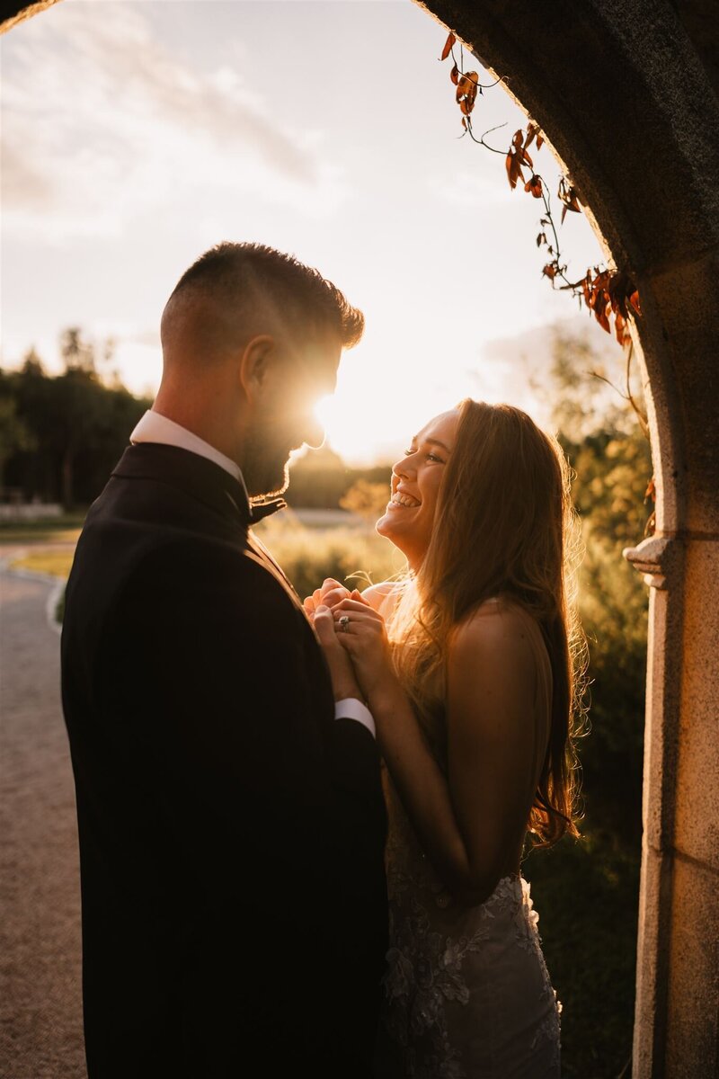 Bride and groom smiling at each other under golden sunset light at Royle Forest Wedding Venue in Derby, holding hands and sharing a joyful moment.