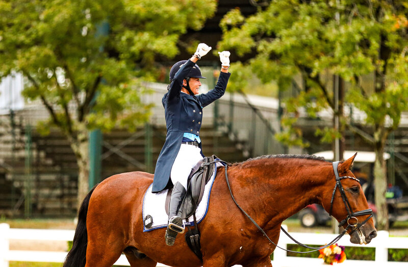 A rider pumping her arms in the air after a dressage test on her bay horse at the Region 3 Championships in Georgia.