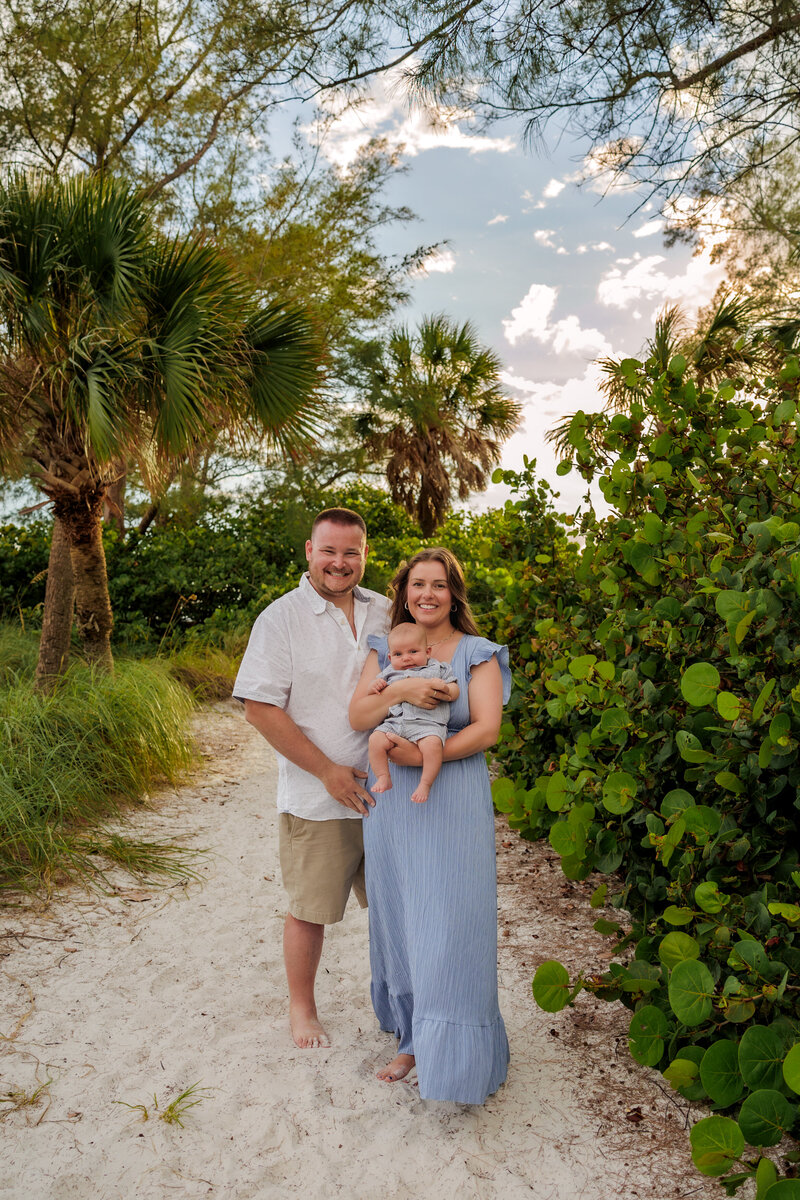 family of three. Mother is holding the baby in front of her while dad puts his hand on her hip.