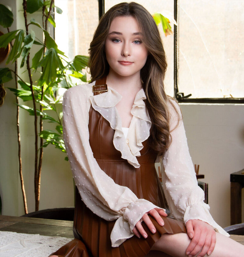 Personal Preteen branding portrait Frankie Jensen sitting with hands on knee in white blouse with frilly collar and brown dress